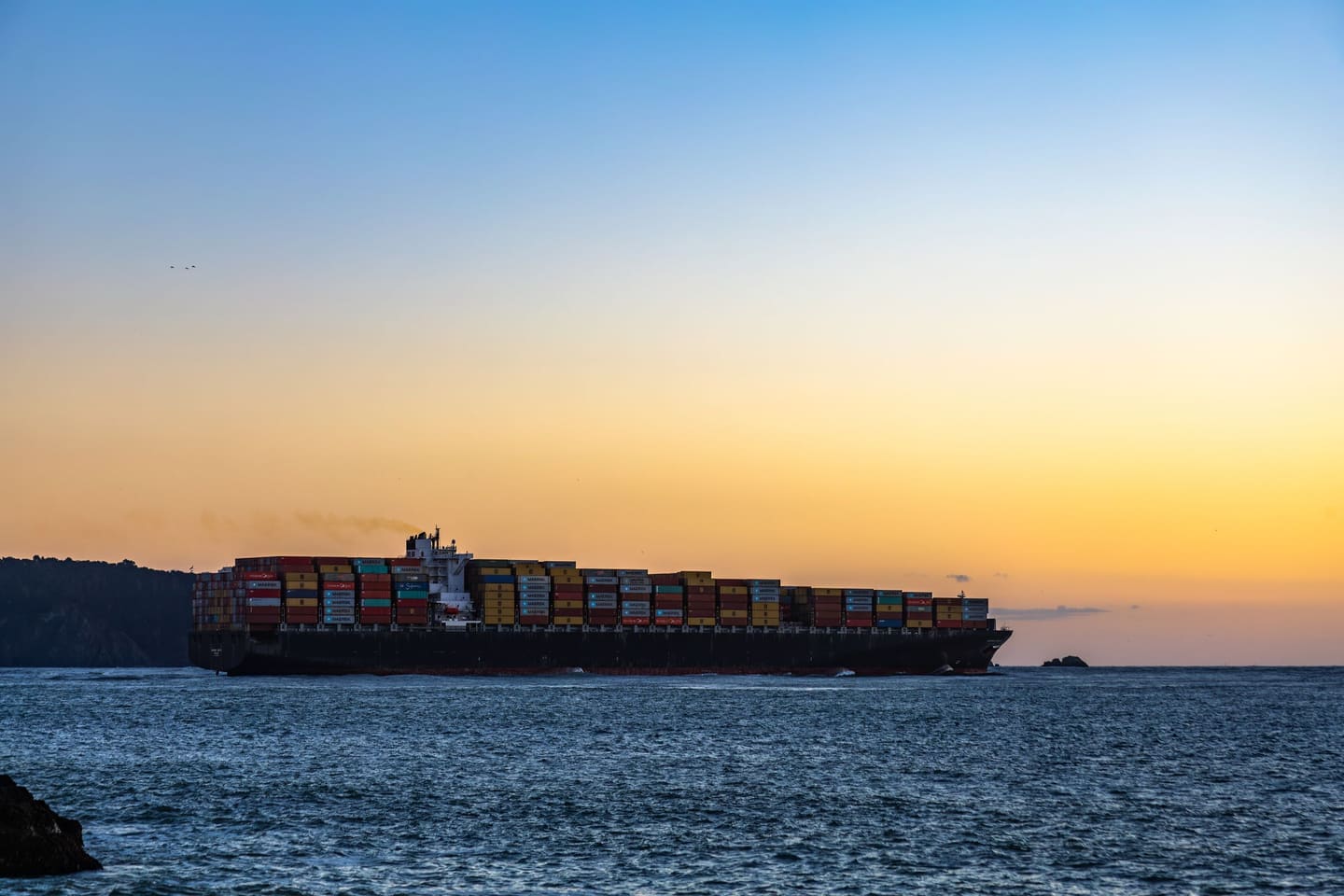 A container ship crossing at dusk, the sea navy, the sky amber