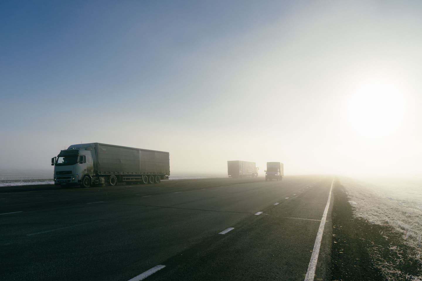 Trucks on an open highway at sunrise, the sun ahead in the mist